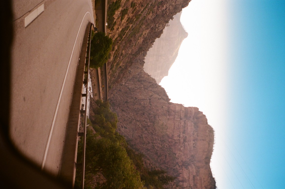 A scene of a river running alongside a road, winding through a rocky valley.